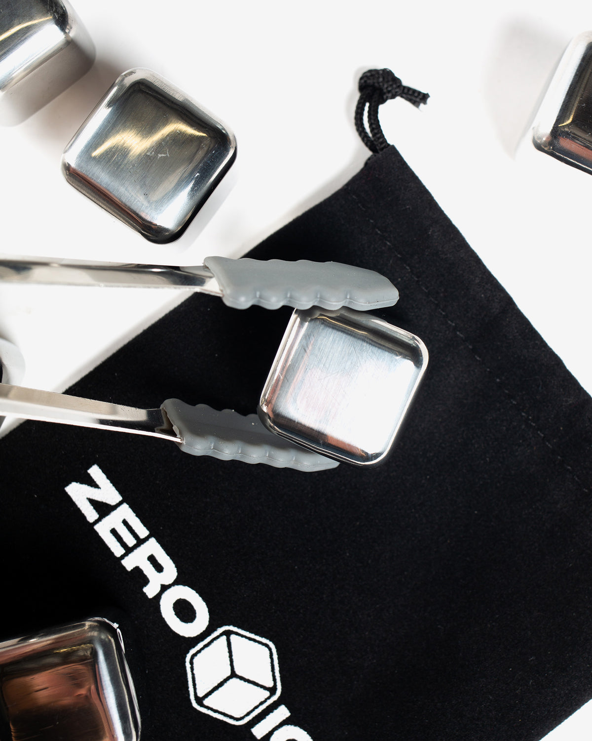 Metallic ice cube trays with silicone handles on a black Zero Ice branded mat.